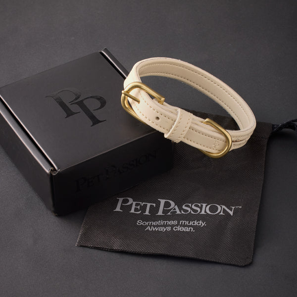 White pet collar with gold buckle on a black box and towel with 'Pet Passion' branding.