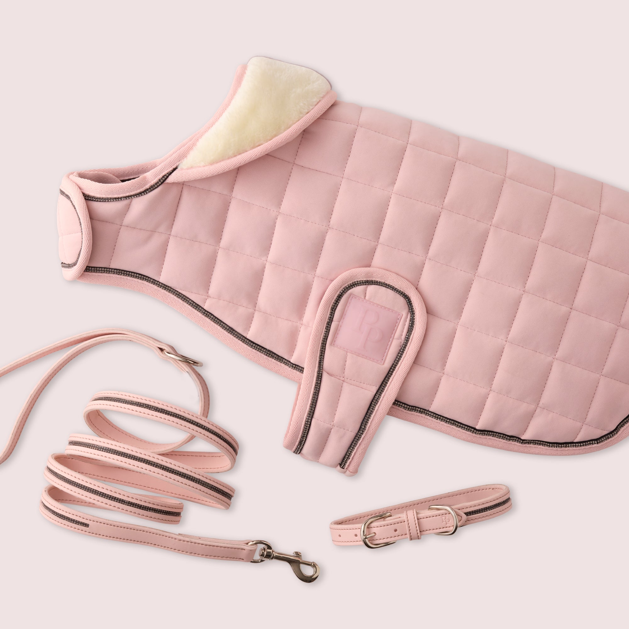 Pink quilted dog coat with matching leash and collar on a light pink background