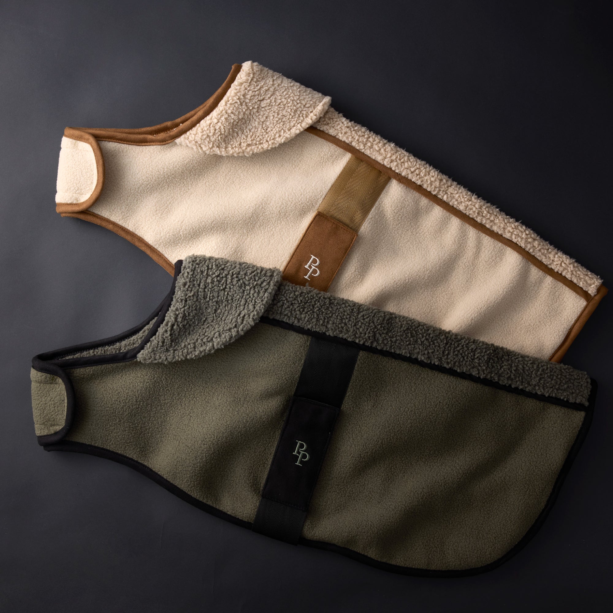 Two dog vests in beige, brown, and green on a dark background