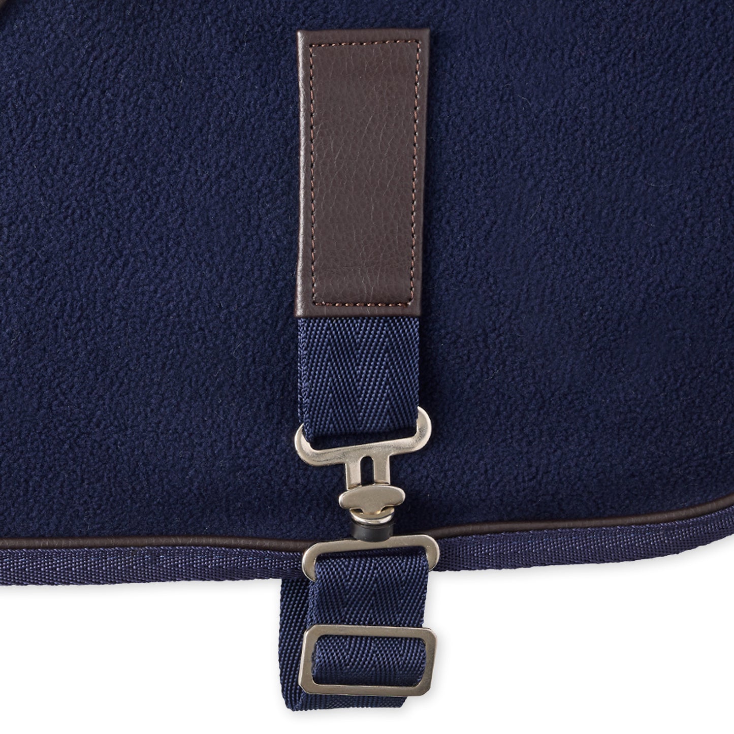 Close-up of a navy blue bag with a brown strap and metal buckle on a white background