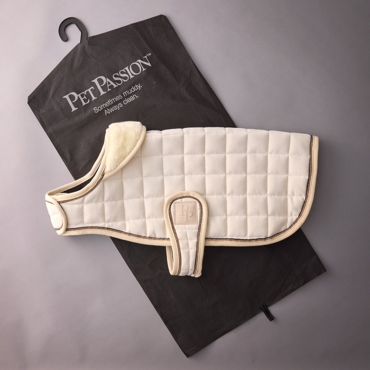 White quilted dog coat on a black towel with 'Pet Passion' branding.