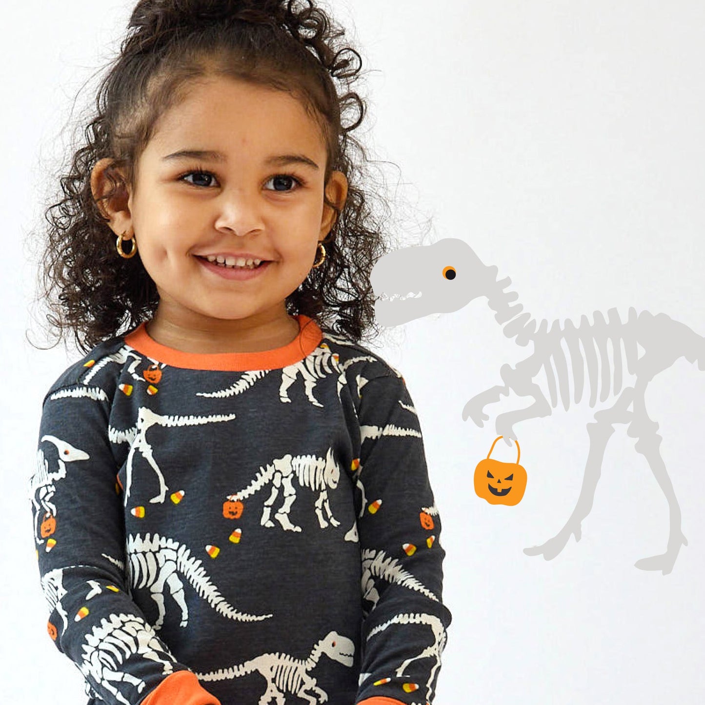 Child wearing a dinosaur-themed shirt with Halloween elements on a white background
