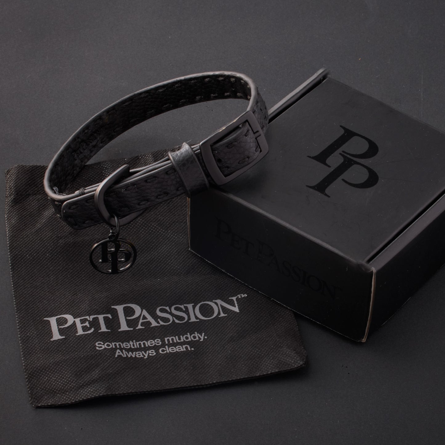 Rein collar in Black Beatuy with it's garment bag and packaging box, labeled with the Pet Passion logo and slogan, all on a black background

