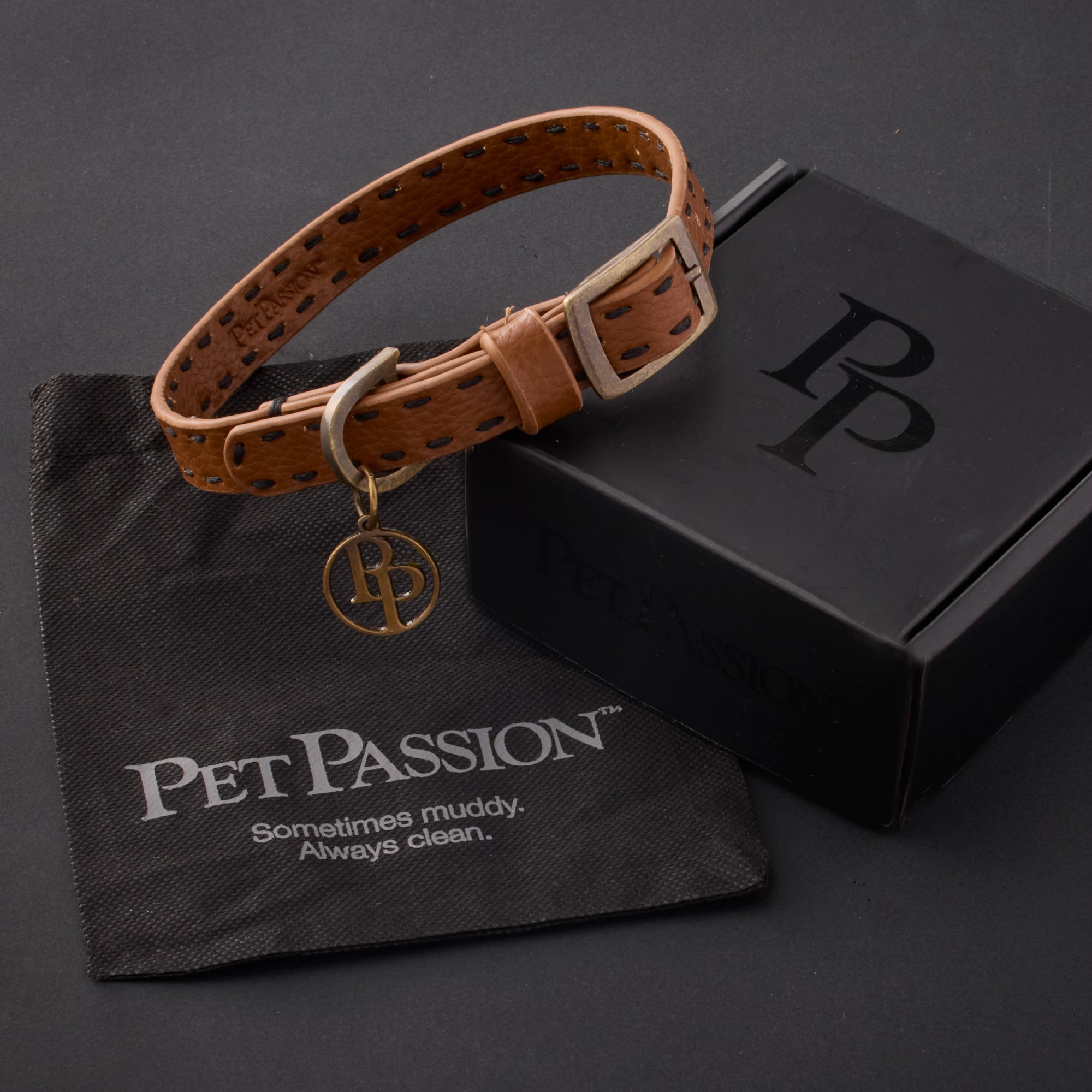 Rein collar in Chestnut Hunter with it's garment bag and packaging box, labeled with the Pet Passion logo and slogan, all on a black background
