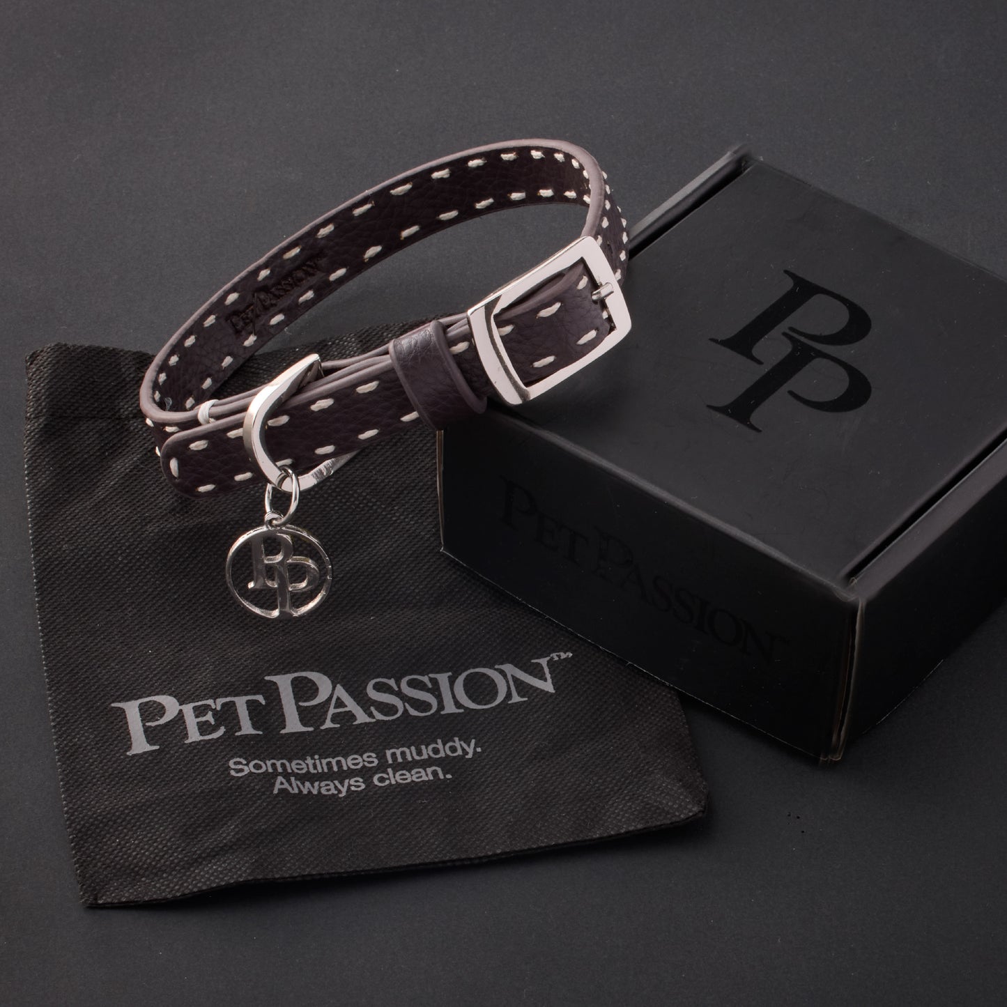 Rein collar in Chocolate Espresso with it's garment bag and packaging box, labeled with the Pet Passion logo and slogan, all on a black background
