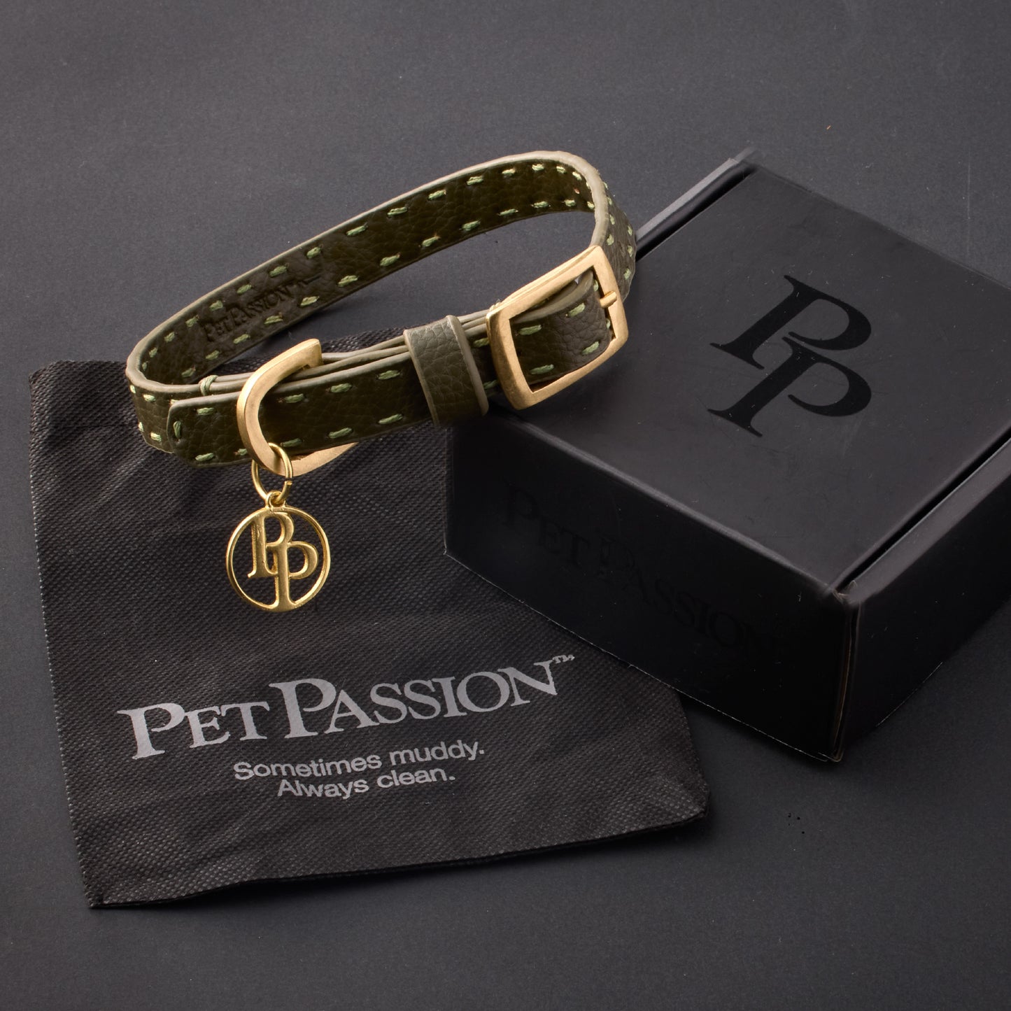 Rein collar in Scottish Olive with it's garment bag and packaging box, labeled with the Pet Passion logo and slogan, all on a black background
