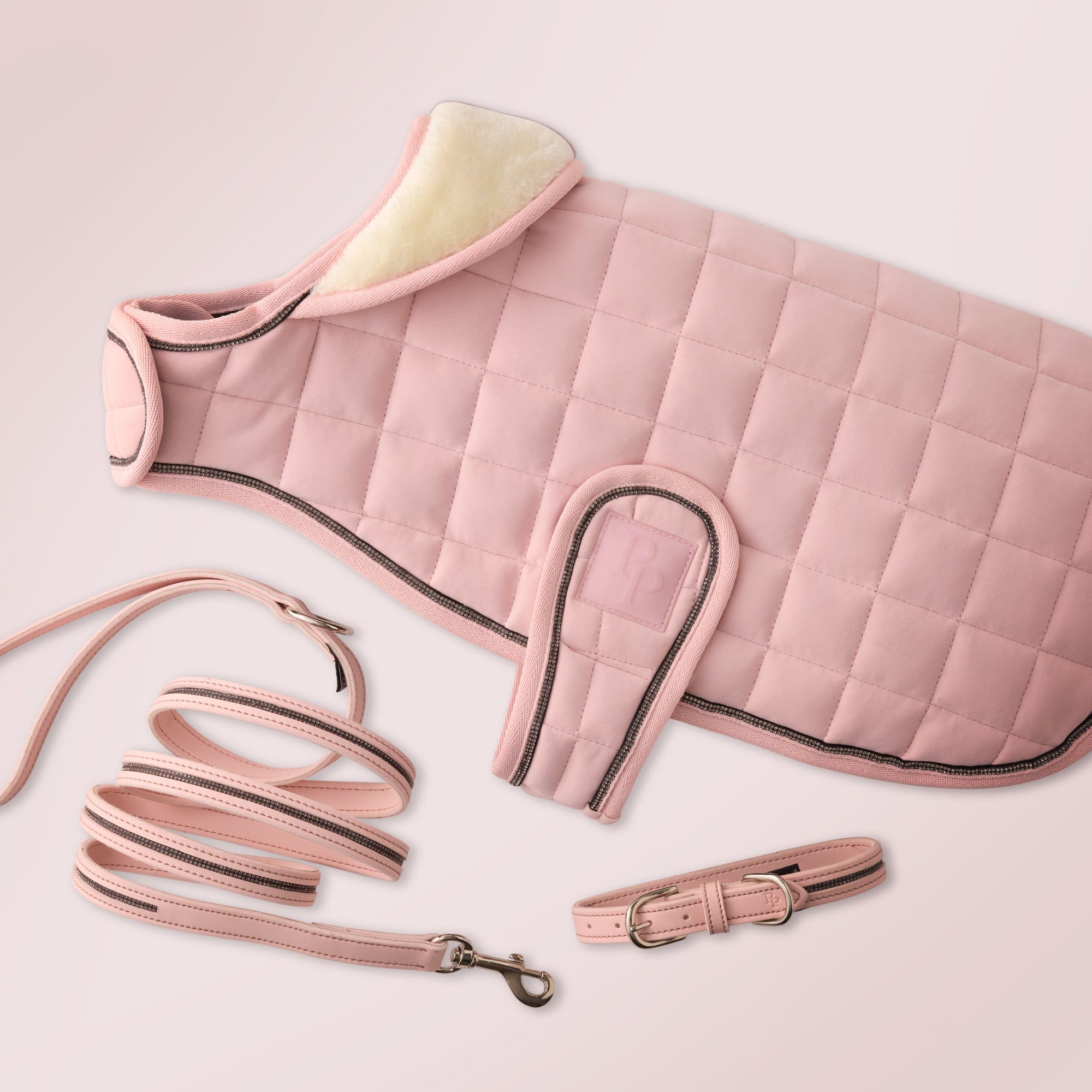 Pink quilted dog coat with matching leash and collar on a light pink background