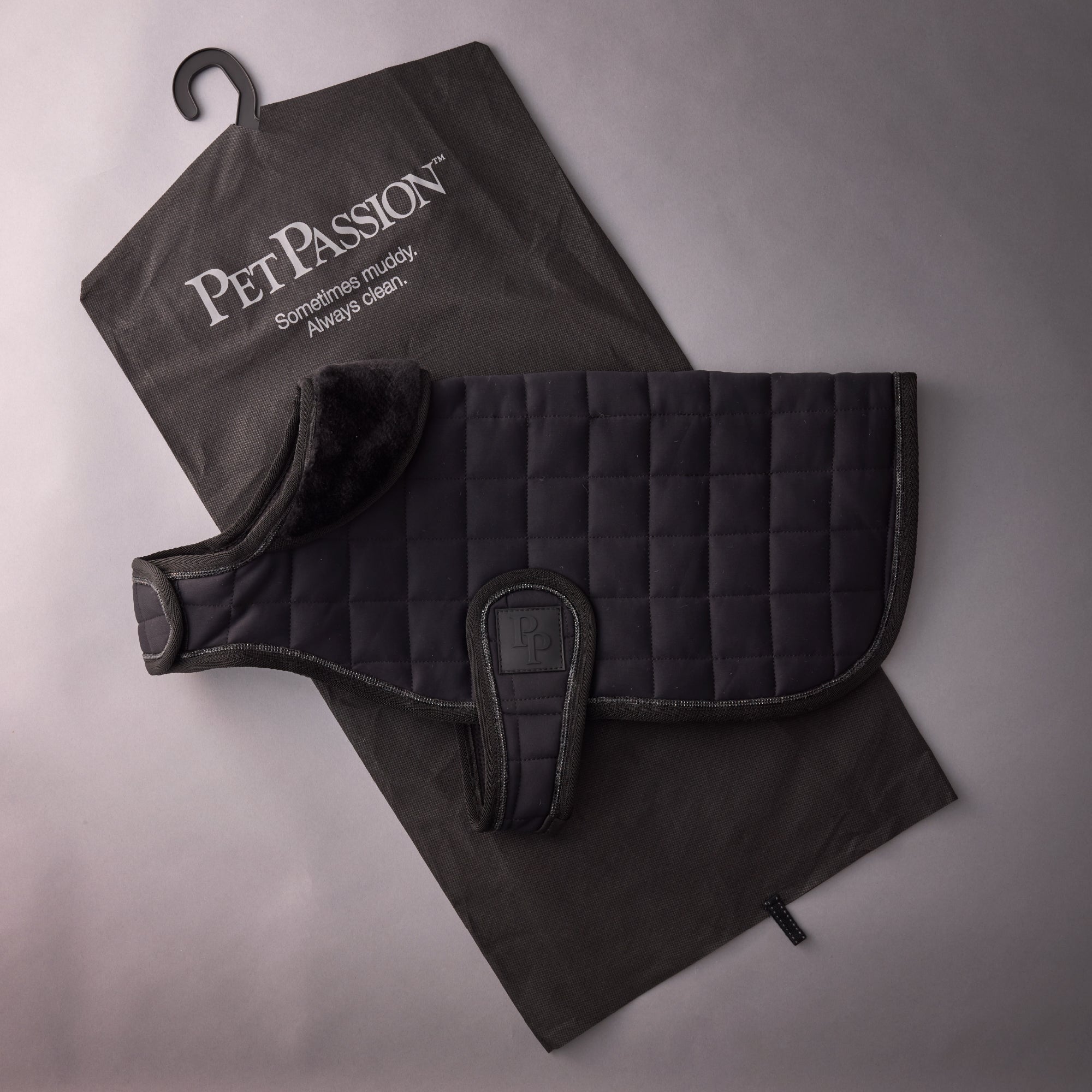 Black quilted dog coat with a towel on a gray background, featuring 'Pet Passion' branding.
