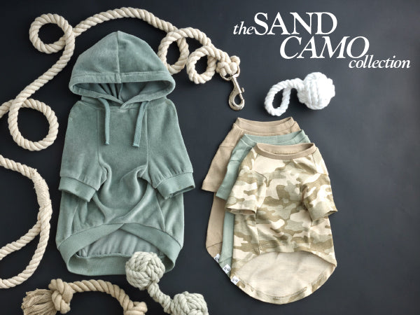 Two baby rompers, one green and one sand camo, on a dark background with ropes.